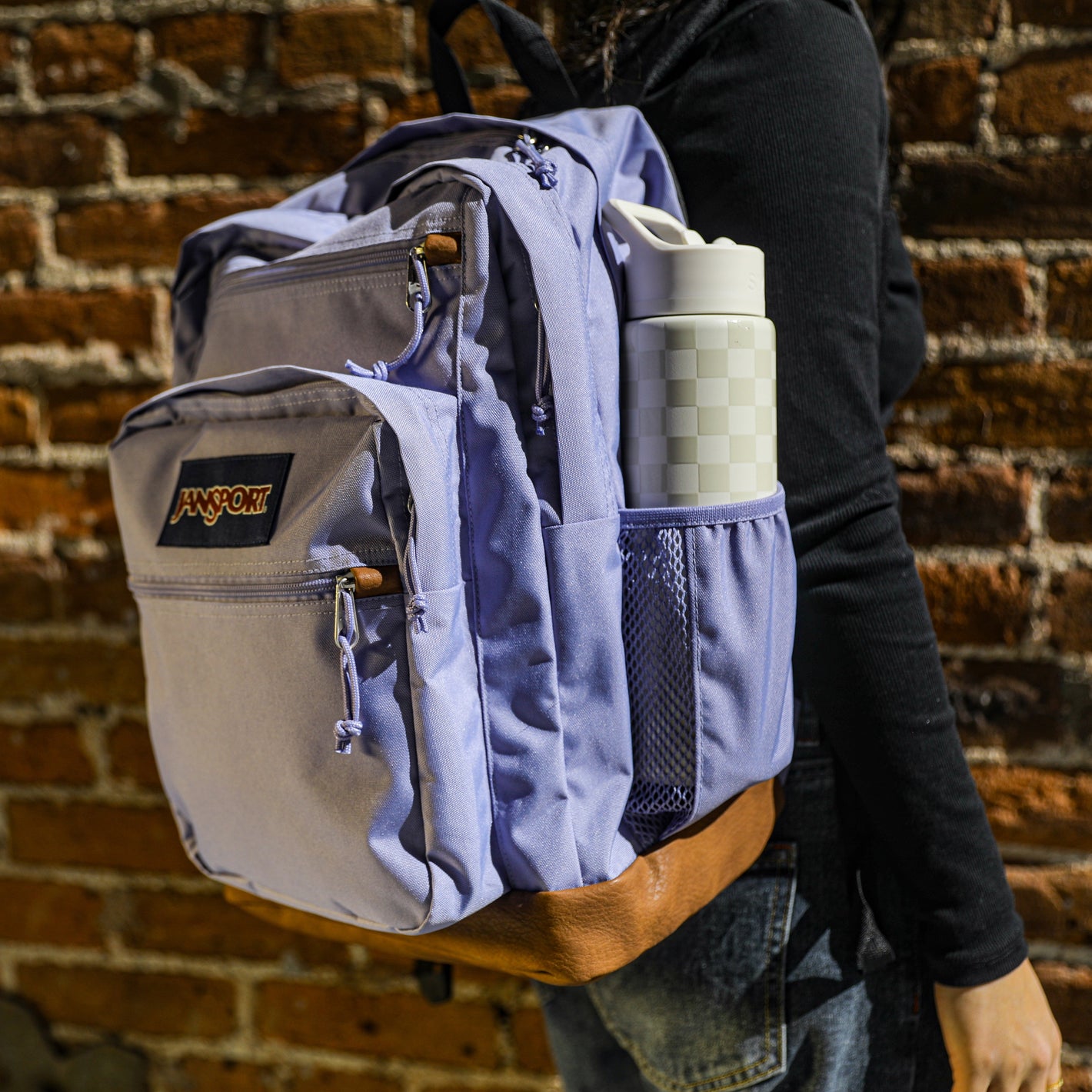 Person wearing a purple jansport backpack with visible brand logo against a brick wall.