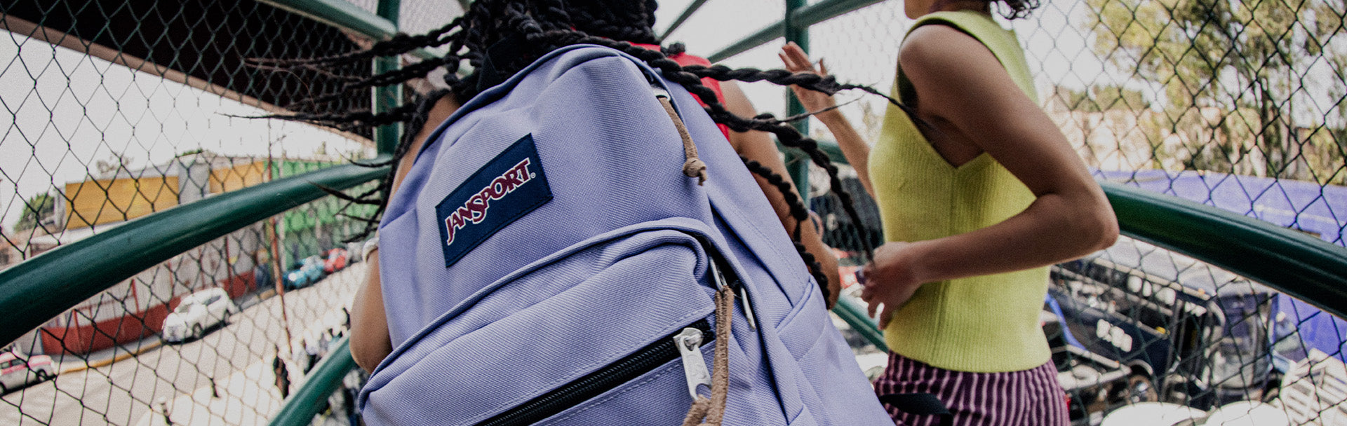 Person with a purple JanSport backpack standing next to a fence with a view of a construction site.