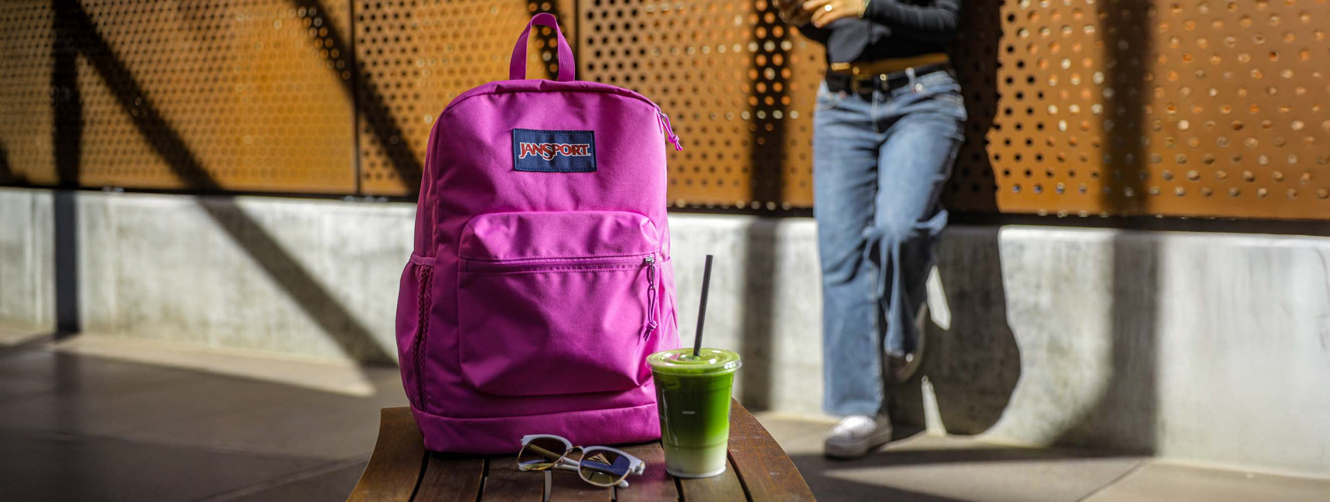 Purple Cross Town Plus backpack on a table next to an iced matcha latte with a person standing in the background