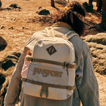 Person wearing a beige backpack with 'Jansport' branding in a natural setting.