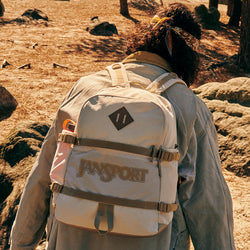 Person wearing a beige backpack with 'Jansport' branding in a natural setting.