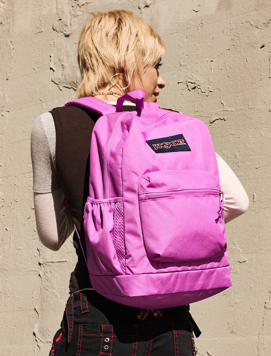 Person wearing a purple backpack with a visible JanSport Logo against a textured wall.