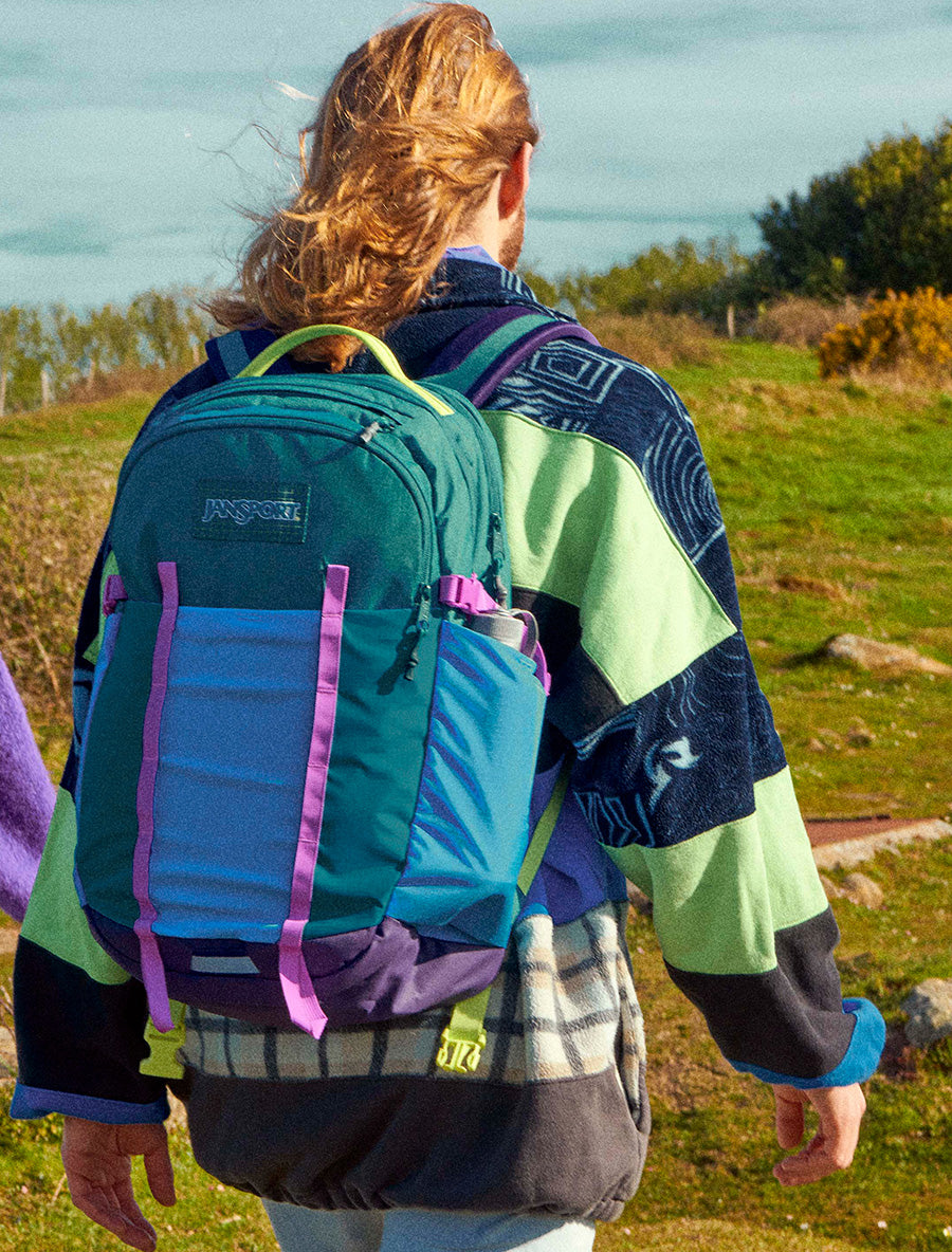 Person wearing a colourful JanSport All Around backpack in an outdoor setting