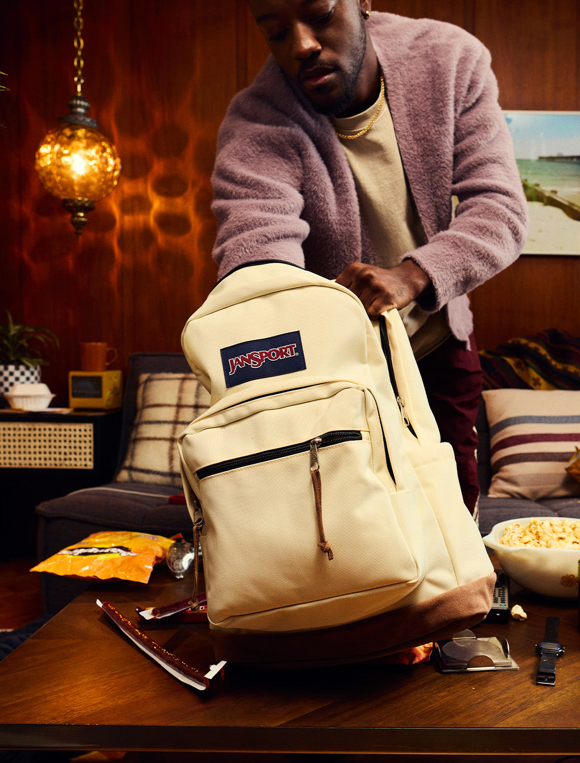 Person opening a beige JanSport backpack in a cozy living room.