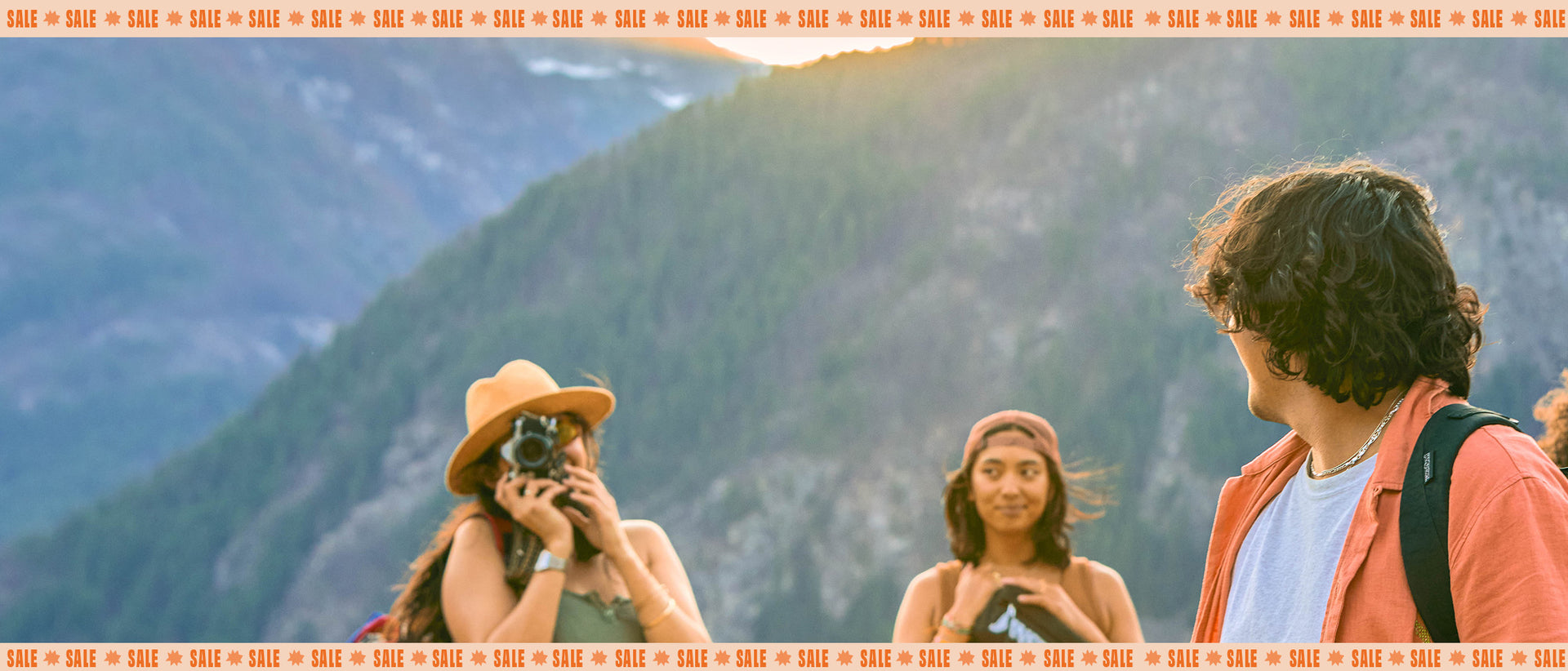Two people taking a photo of a mountain landscape wearing Jansport backpacks